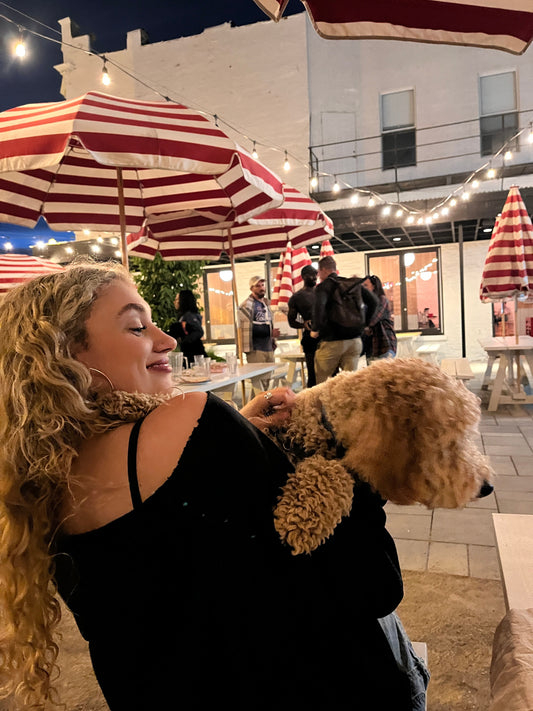 Woman with long 2C wavy hair smiling while holding a curly-haired dog at an outdoor café